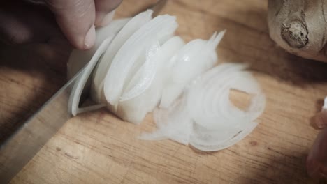 chef's hand rapidly cutting white onions on wooden chopping board with knife