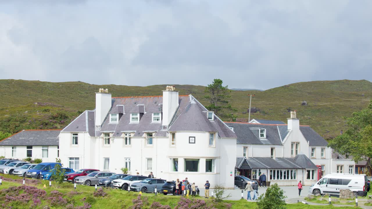 Wide shot of traditional white clubhouse hotel with people and cars, set in green hills