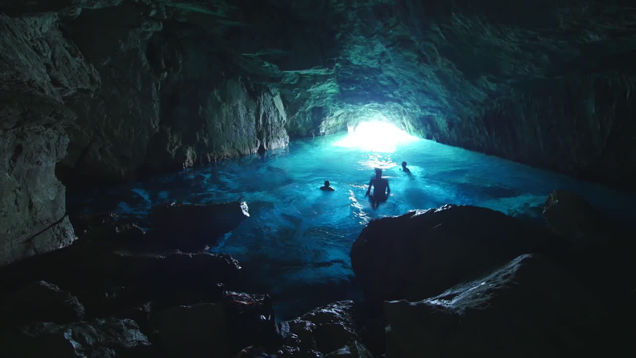 tres hombres saltando en el agua dentro de una cueva azul en las calancas. marsella