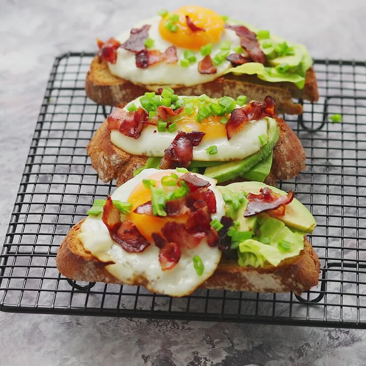 Tasty delicious homemade toasts with fried egg bacon avocado lettuce and chive Served on grill
