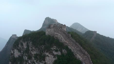 Fly-over-old-part-of-Great-Wall-of-China-with-deteriorate-lookout-tower-on-top-of-mountain-on-a-cloudy-day