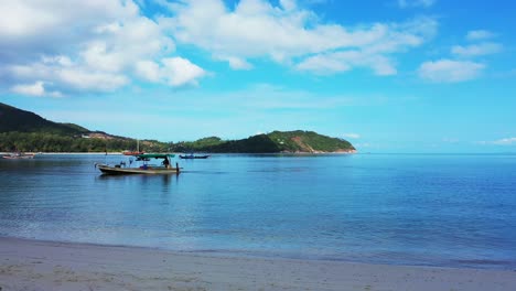 fishing boat anchoring on calm lagoon washing sandy beach of tropical island, bright blue sky with white clouds in thailand