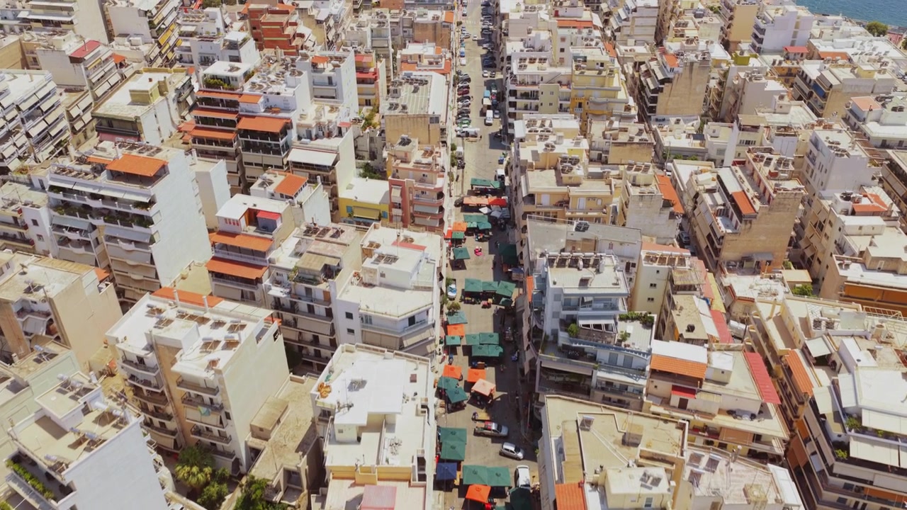 Vista aerea della vivace città del Pireo, Grecia, che sorvola il denso paesaggio urbano e il vibrante mercato di strada di Kallipoleos con le sue bancarelle colorate che si estendono verso il mare