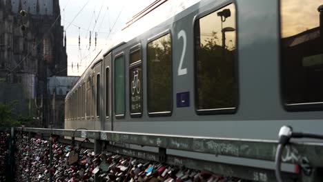 regional train going past railing with padlocks during golden hour in cologne