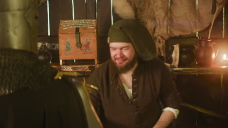 barkeeper blows in straw and decorates drink for knight in tavern. busy dwarf innkeeper treats alcohol for noble pilgrim in best way at bar counter