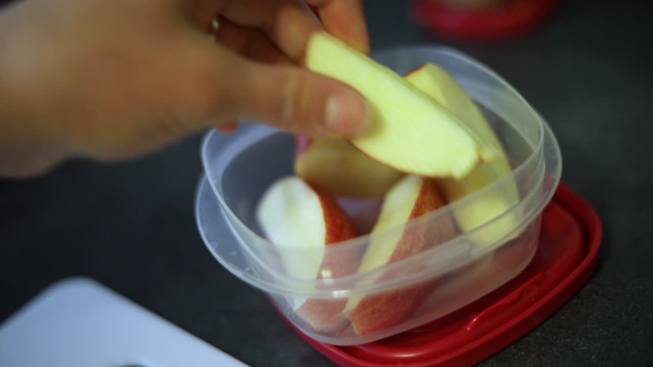 toma en cámara lenta de alguien poniendo rodajas de manzana recién cortadas en un pequeño recipiente de tupperware