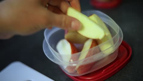 slow motion shot of someone putting freshly cut apple slices into a small tupperware container