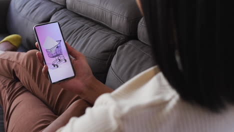mujer biracial en el sofá usando teléfono inteligente para comprar en línea, cámara lenta