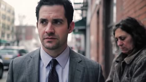 a moment of reflection: a well-dressed man on the sidewalk passes a woman in distress, capturing the contrast of their lives