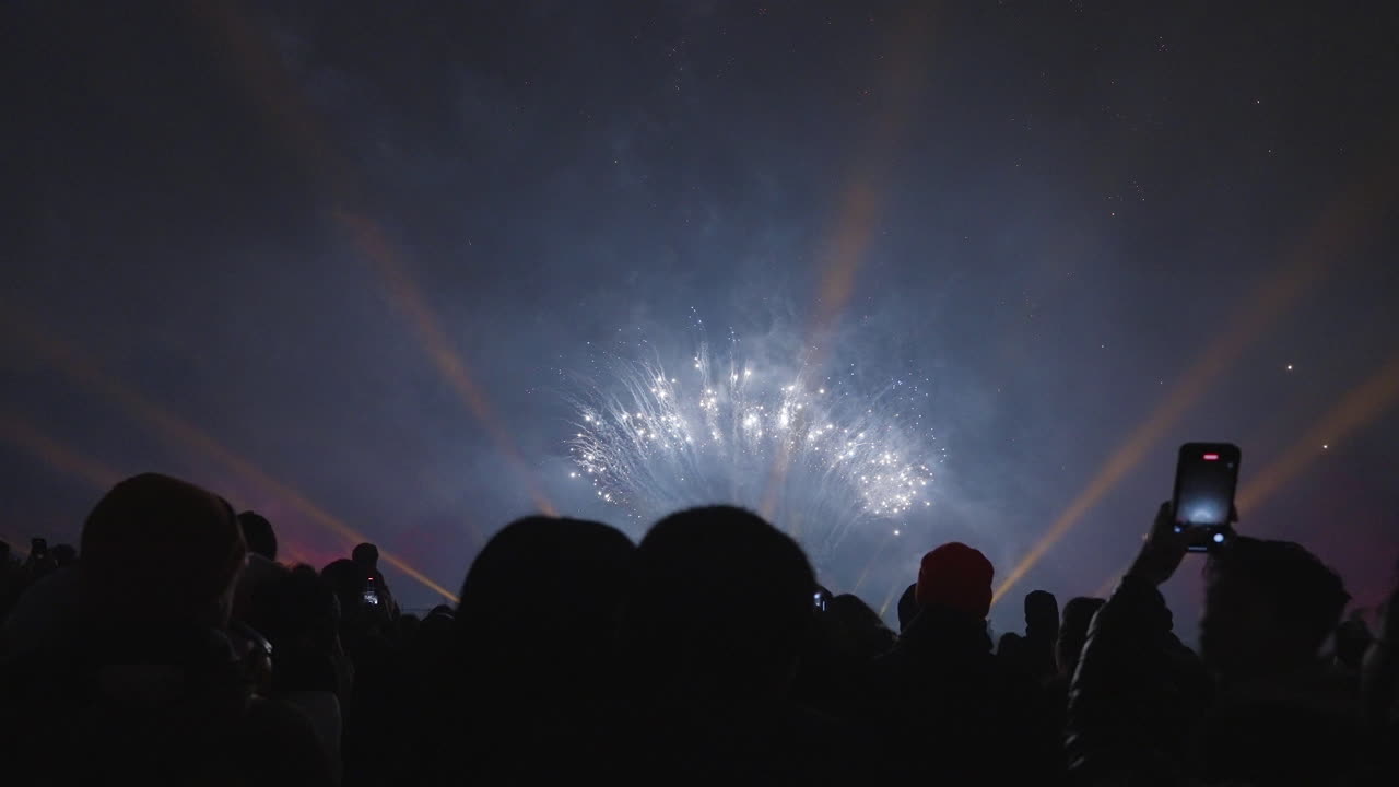 People filming colorful fireworks against a dark sky