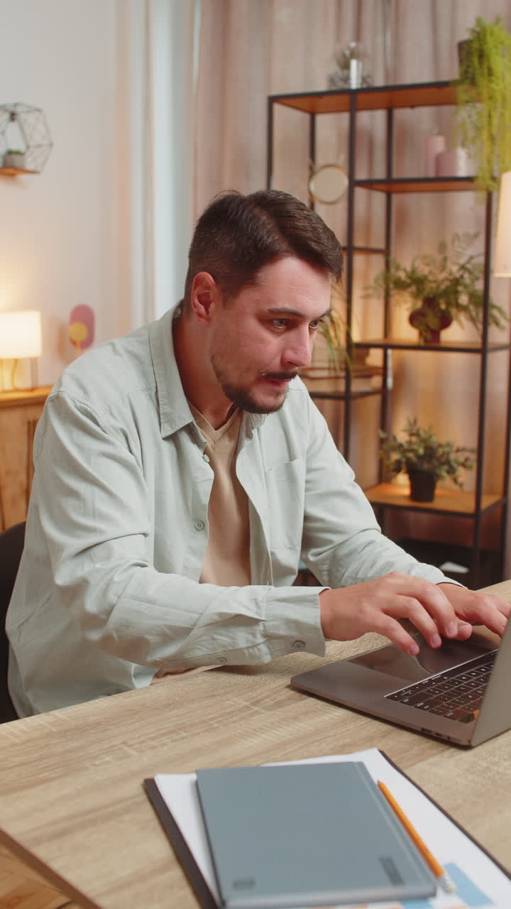 Happy young caucasian man working on laptop shocked by sudden victory sitting at home office table