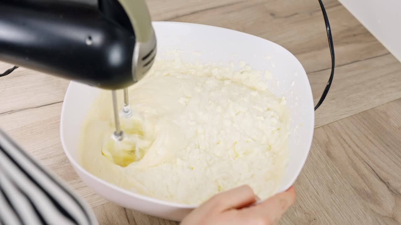 Mixing mascarpone and cream with hand mixer during tiramisu dessert preparation, careful movement