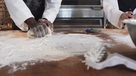 Diverse-bakers-working-in-bakery-kitchen,-kneading-dough-on-counter-in-slow-motion