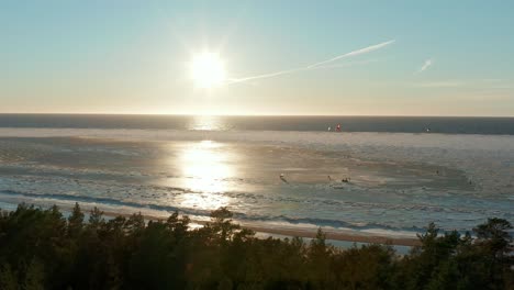 group of people kitesurfing with ice skates over a frozen part of baltic sea during a sunny day