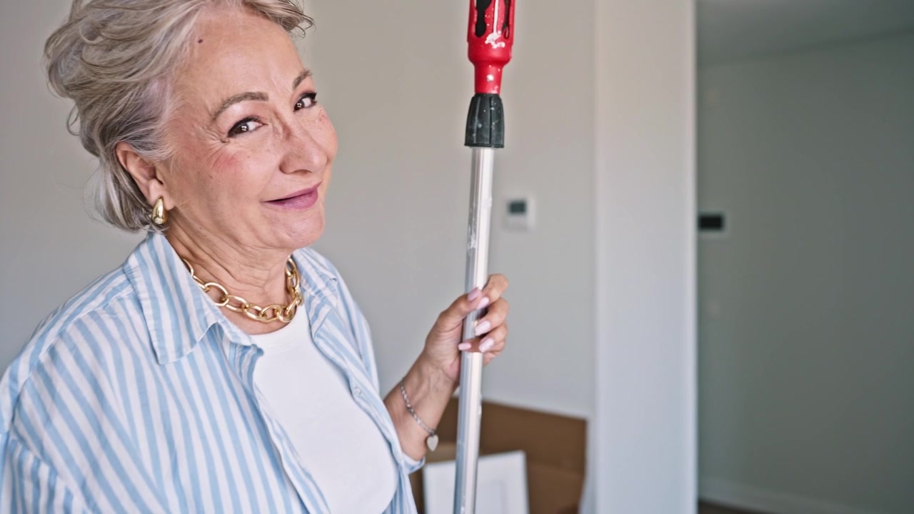 Donna anziana allegra con rullo da pittura e secchio nella nuova casa