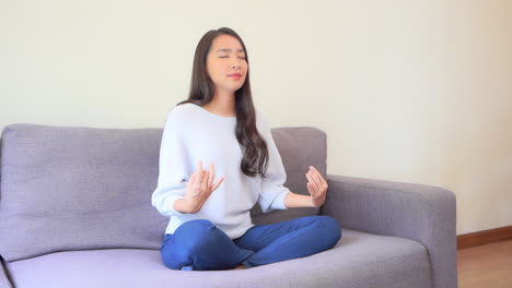 pretty asian girl practicing relaxing yoga at home on the sofa slomo