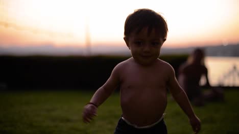 latin shirtless baby boy walking on the grass having fun at dusk
