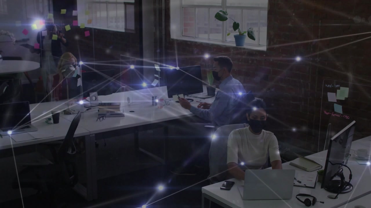 Seated woman working laptop in office while colleague walking across to join team, overlay pulsing