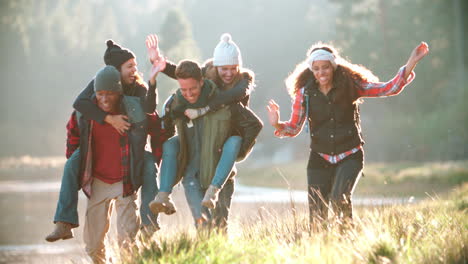 five friends have fun piggybacking by a rural lake