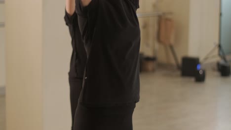 검은색 댄스웨어를 입은 젊은 발레 학생들이 나무 바닥과 벽에 장착된 바를 가진 넓은 발레 스튜디오에서 자세를 연습하는 그룹.