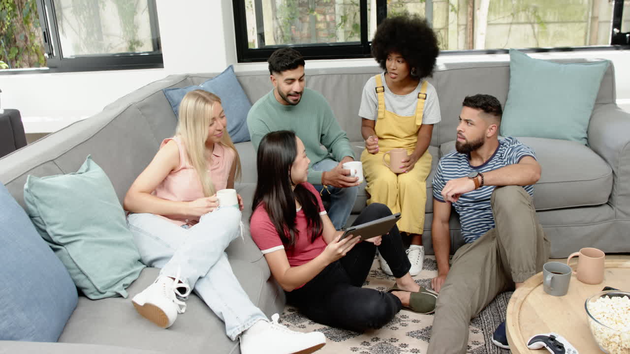 Gathering on couch, group of young friends chatting and enjoying coffee together