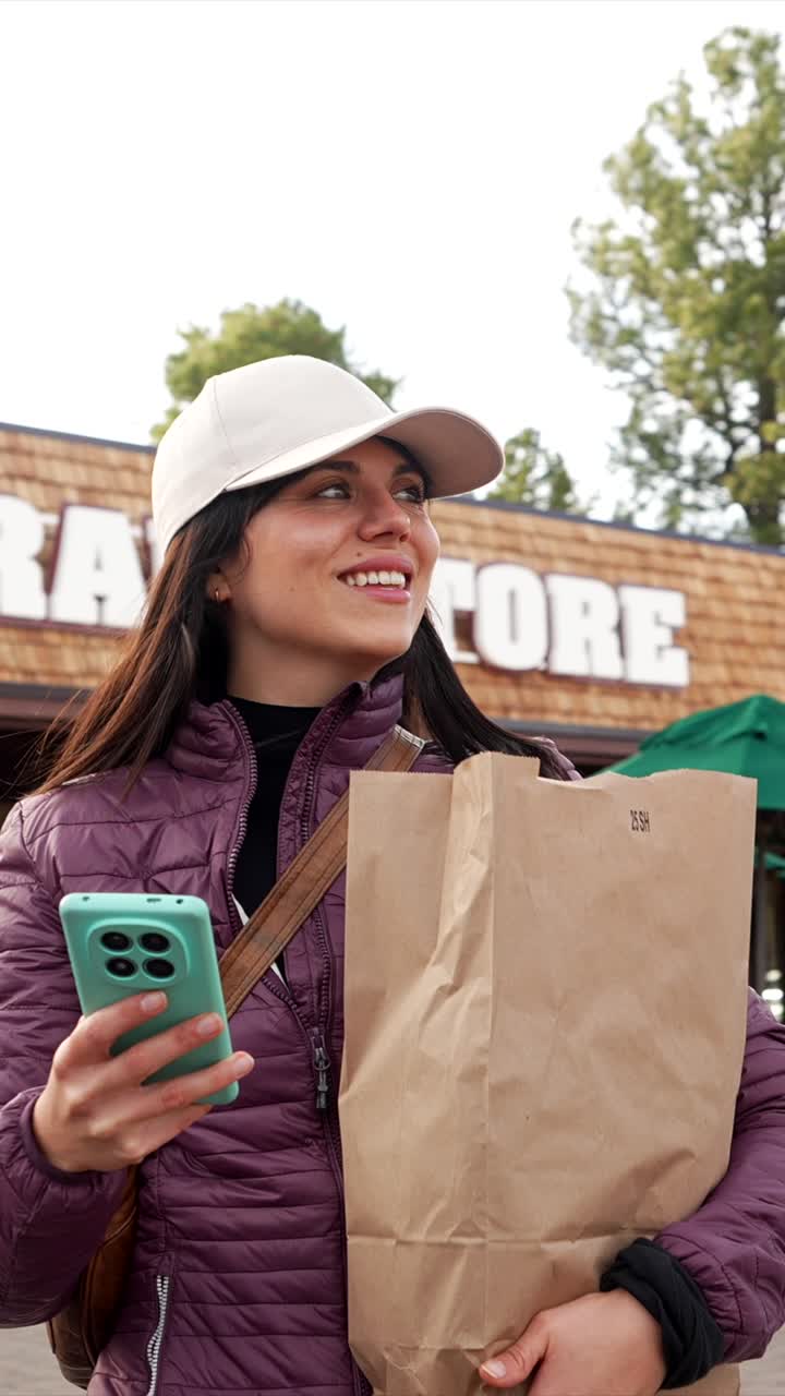 Happy Young Woman Holding Shopping Bag and Smartphone Outside Store