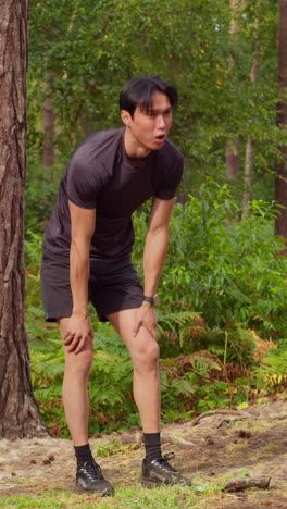 vertical video of tired man exercising doing work out outdoors running along track through forest stopping to catch breath shot in real time