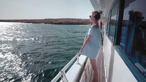 portrait of a young beautiful sexy caucasian woman on a yacht in in a blue dress and sunglasses looks at a deserted island. the concept of vacation, freedom, sunny summer. blue ocean on backgroung. steadycam