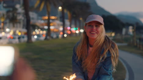 Junge-Frau-Tanzt-Lustig-Mit-Wunderkerzen.-Freund-Macht-Fotos-Mit-Smartphone-Kamera-Und-Teilt-Silvesterfeier-Am-Strand-Bei-Sonnenuntergang