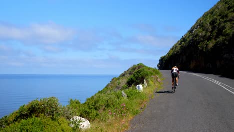 female cyclist cycling on a coastal road on a sunny day 4k