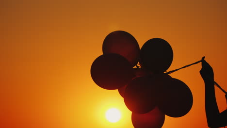 Eine-Hand-Hält-Mehrere-Ballons-Bei-Sonnenuntergang