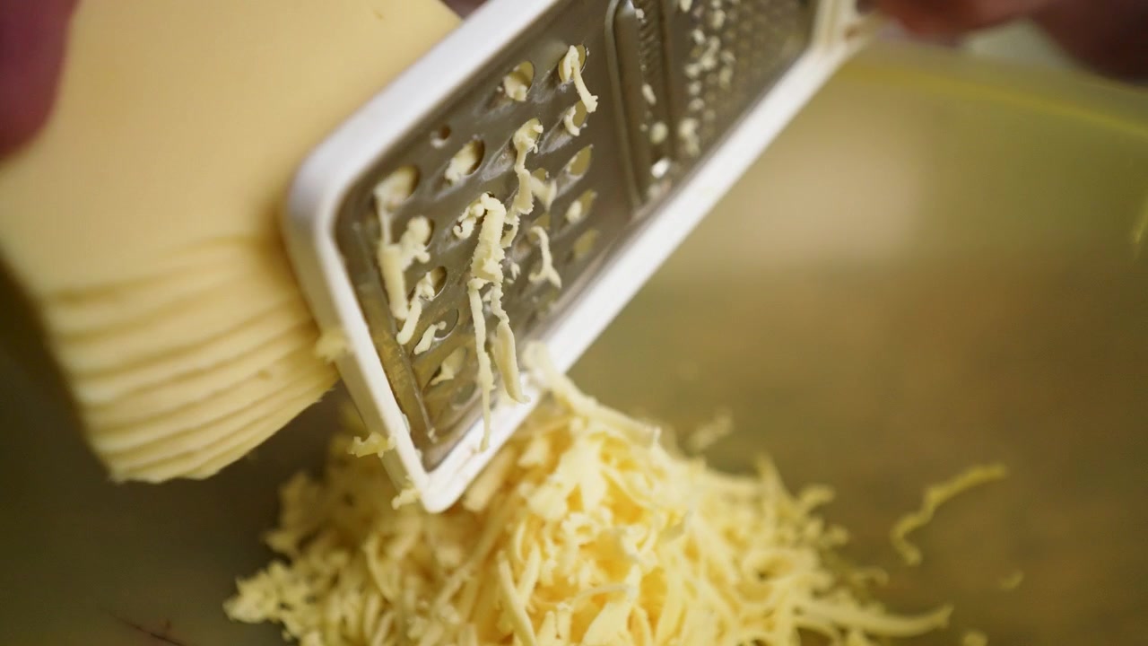 Primo piano di uno chef che grattugia formaggio fresco, mostrando la consistenza e il movimento.