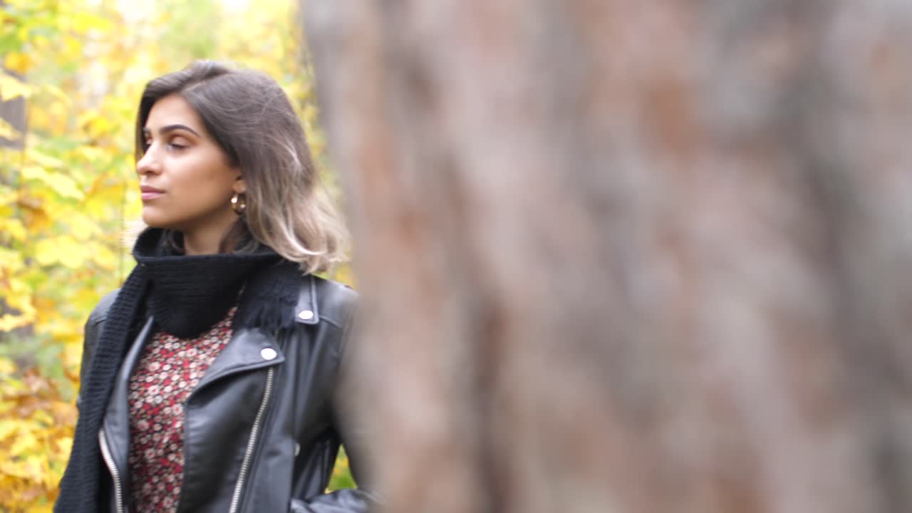 Wide shot of Brunette girl in autumn forest, stands thoughtfully and looks straight - The camera pans to the side and a tree appears as a transition