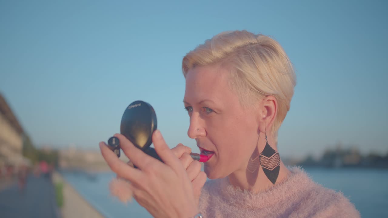 Donna vivace di mezza età che si sistema il rossetto all'esterno usando uno specchio portatile. Primo piano, rallentatore
