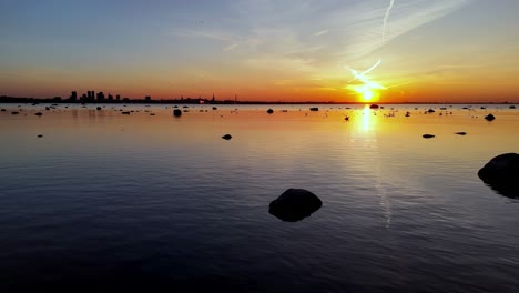 Aerial-scenic-view-of-Tallin-capital-of-Estonia-at-sunset,-drone-fly-above-Baltic-Sea-with-stone-and-reflection