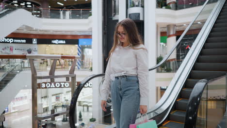 lady steps off descending escalator with shopping bags in hand in bustling modern mall, surrounded by diverse stores and shoppers in background, reflecting vibrant urban consumer lifestyle