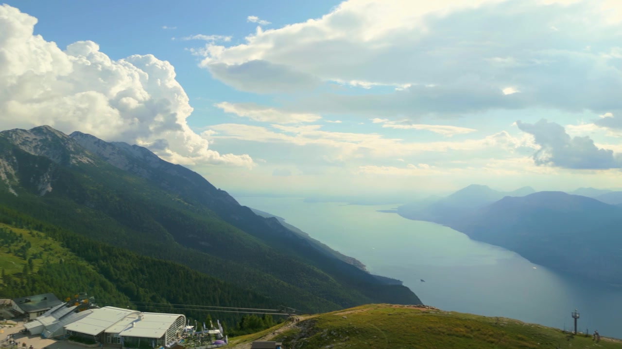 Pemandangan udara luas lereng gunung berumput, lift ski, dan danau besar di bawah