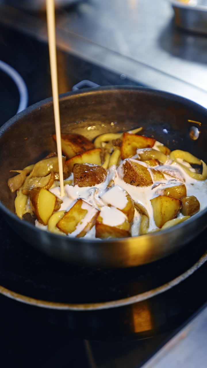 Cream is poured on top of the fried potatoes. Fried vegetables cooked in the frying pan. Close up. Vertical video.
