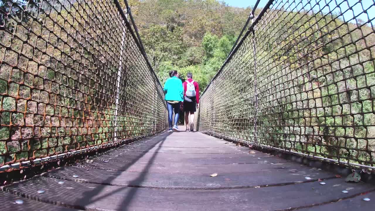 pareja aventurera, hombre y mujer, cruzando un puente colgante en fragas do eume, galicia, durante un día soleado