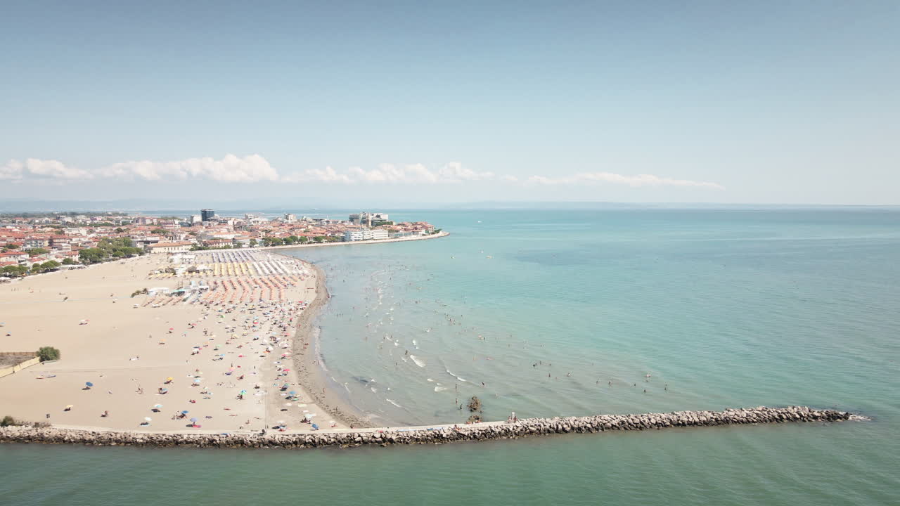 Drone 4K UHD si allontana fluidamente dalla spiaggia sabbiosa di Grado, rivelando un molo in pietra e il vasto Mare Adriatico—ideale per film di viaggio e inquadrature di apertura.