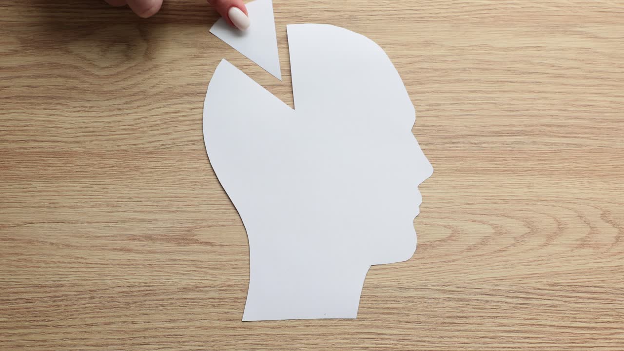 Conceptual image of a hand placing a piece into a human head paper cutout