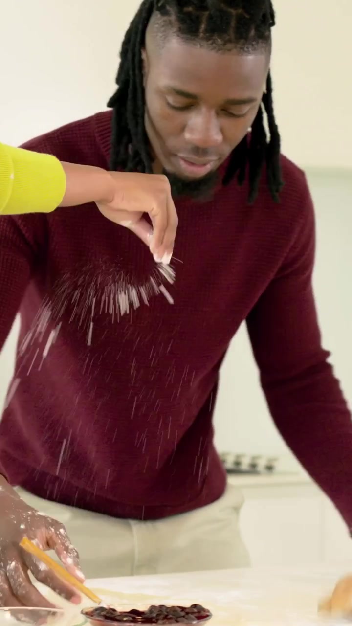 Video verticale: Uomo in marrone che impasta e prepara l'impasto sul bancone della cucina, con un braccio giallo che spolvera farina