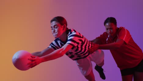Diverse-female-rugby-players-playing-rugby-over-neon-pink-lighting