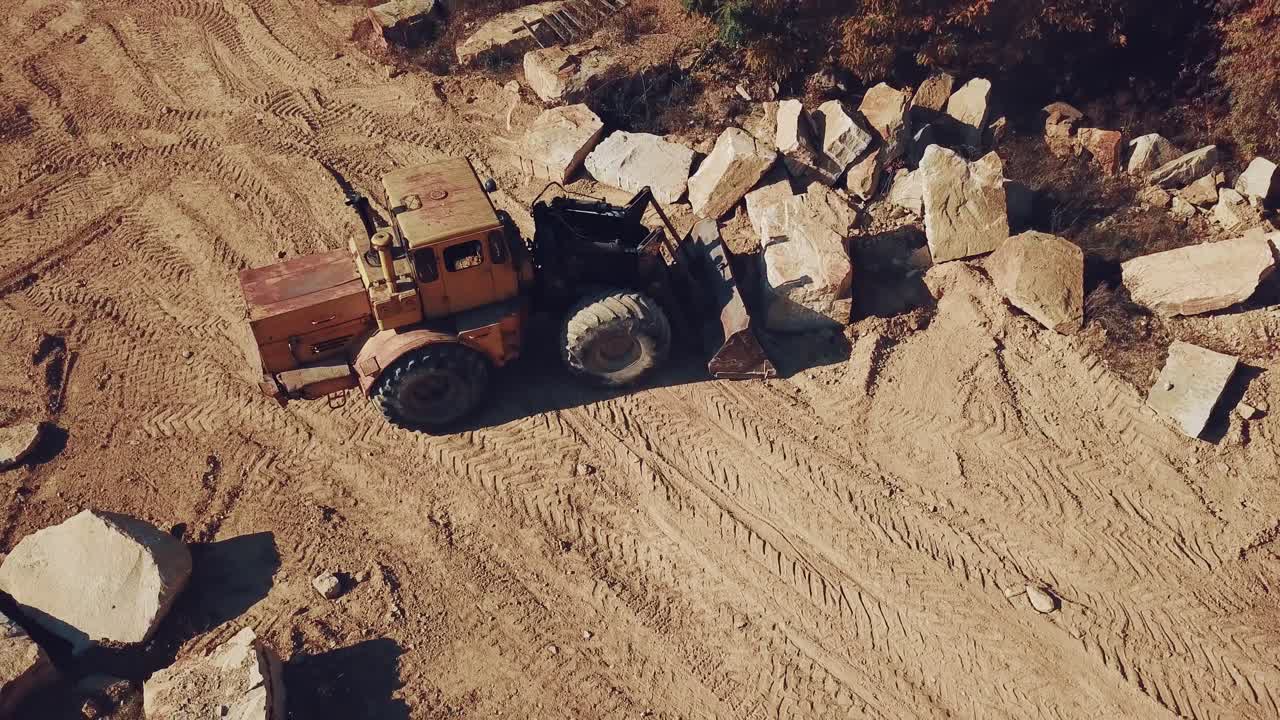 specially equipped bulldozer with a jug is picking up a stone in the quarry on the background of a rock with a forest. View of the sand quarry. Camera motion up.