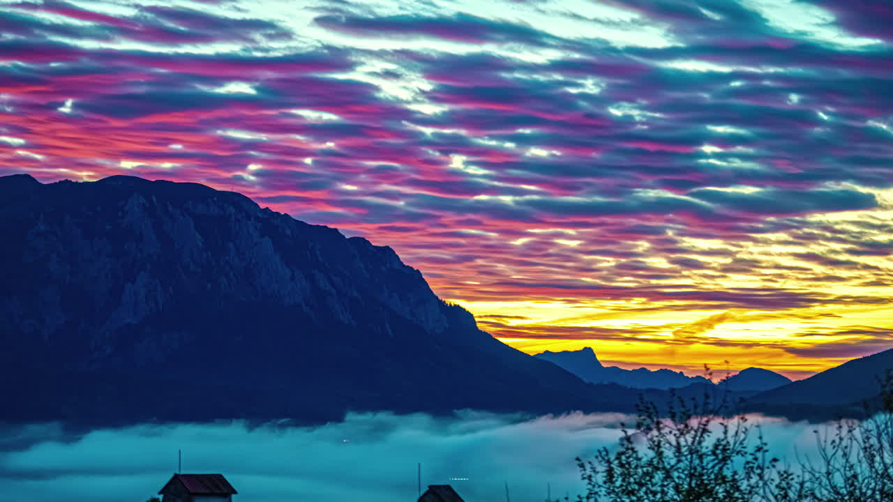 화려한 산과 두꺼운 안개 층 위의 오렌지색 하늘에서 구름에 반사되는 활기찬 은 빛의 불빛 일몰