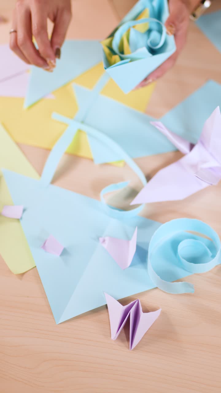 Ripresa dall'alto di mani che organizzano lavoretti di carta pastello e figure di origami su una scrivania.