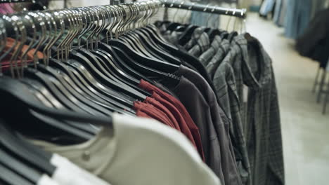 clothing store, captured with a handheld camera, showcasing a close-up of various clothes on hangers, including shirts, jackets, and blouses