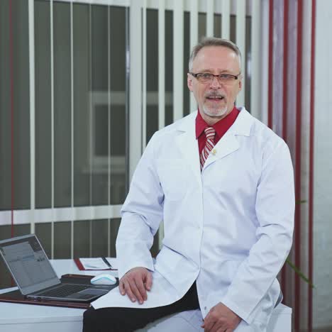 physician recording webinar training. professional male doctor sitting on desk and talking in healthcare center. doctor in glasses and white medical uniform looking at camera.