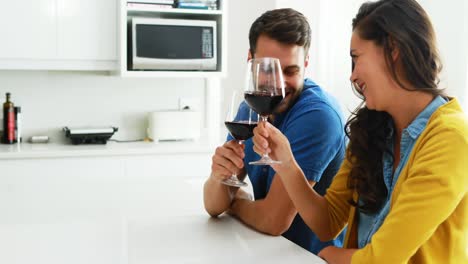 couple interacting with each other while having glasses of red wine in the kitchen