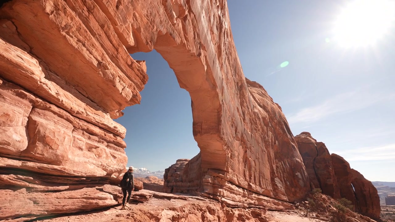 Escursionista con zaino che cammina sotto un arco naturale nel deserto dello Utah, USA